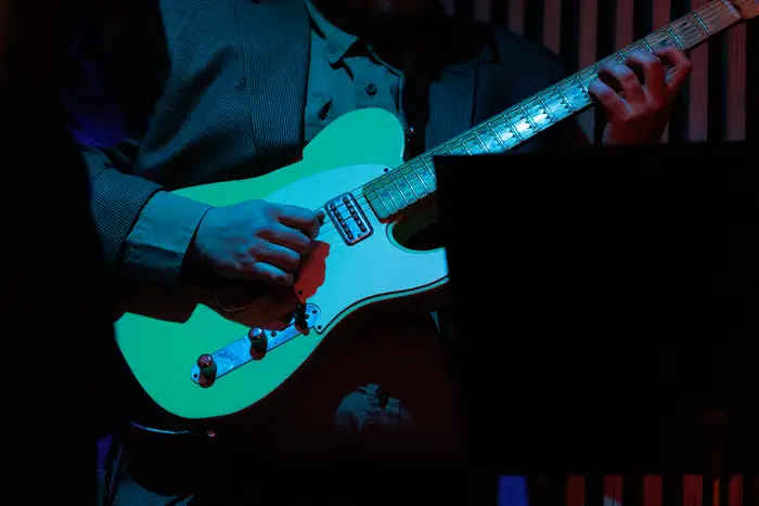 A guitarist playing under stage light, teal guitar catching the colour