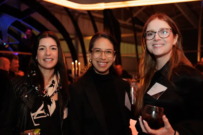 Three guests talking, drinks in hand, under the coloured hangar lighting