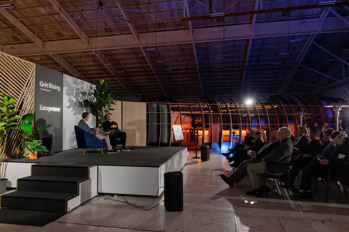 The seated audience from the back of the hangar, stage lit at the far end