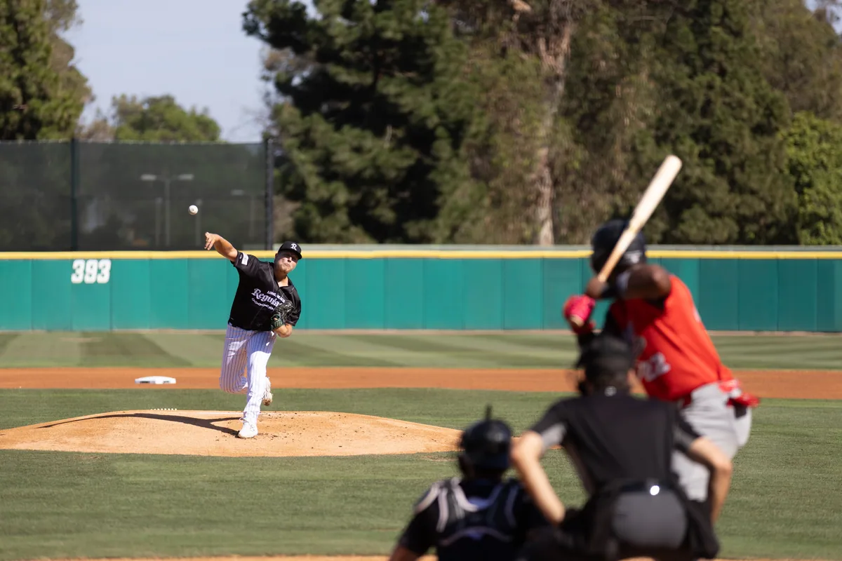 A Regulators pitcher at release, the batter waiting out of focus in the foreground