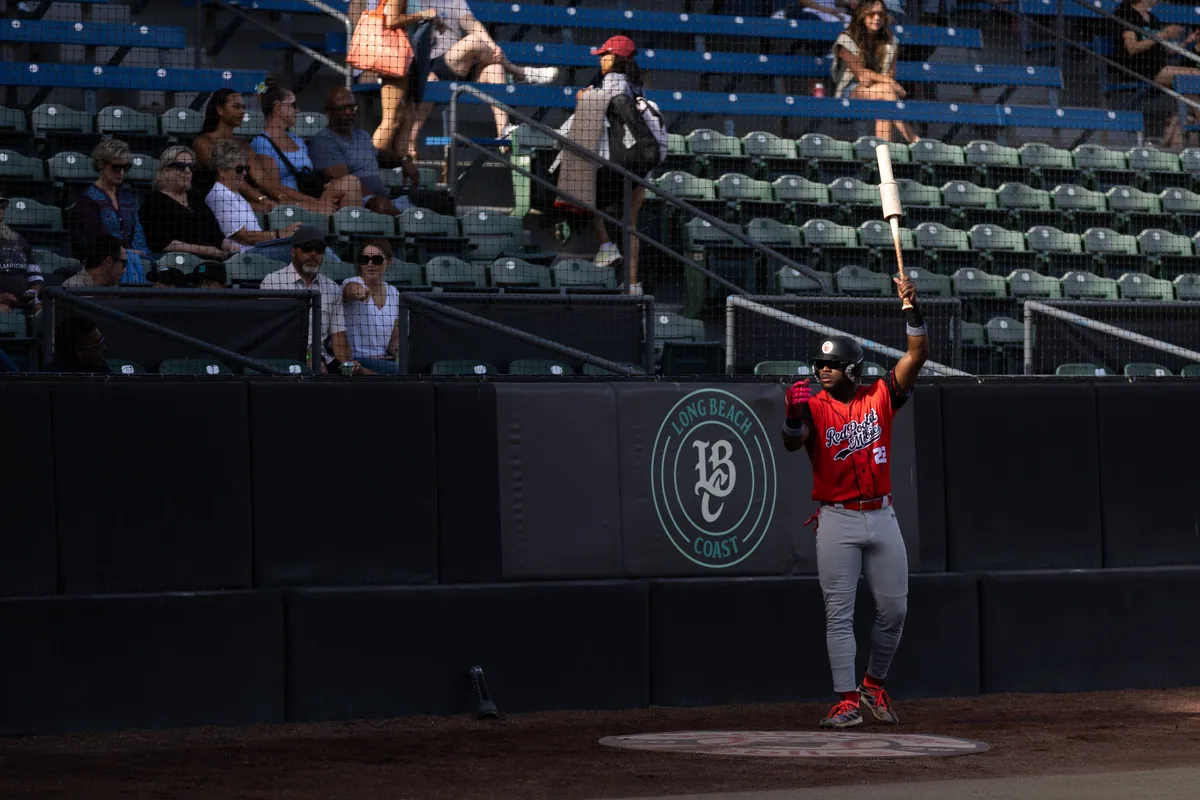 A hitter waits on deck beside the Long Beach Coast roundel