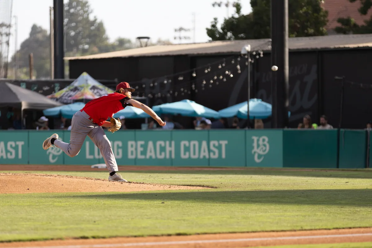 A pitcher follows through in front of the Long Beach Coast wall