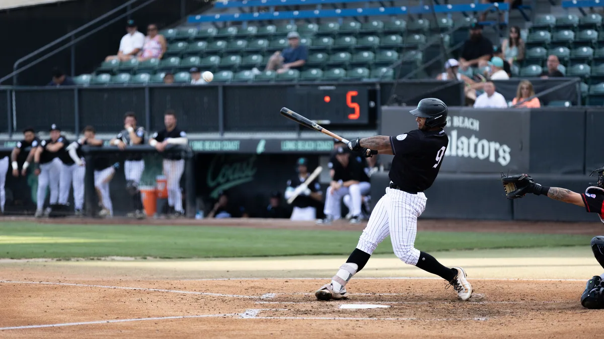 A left-handed swing with the Regulators board behind the backstop