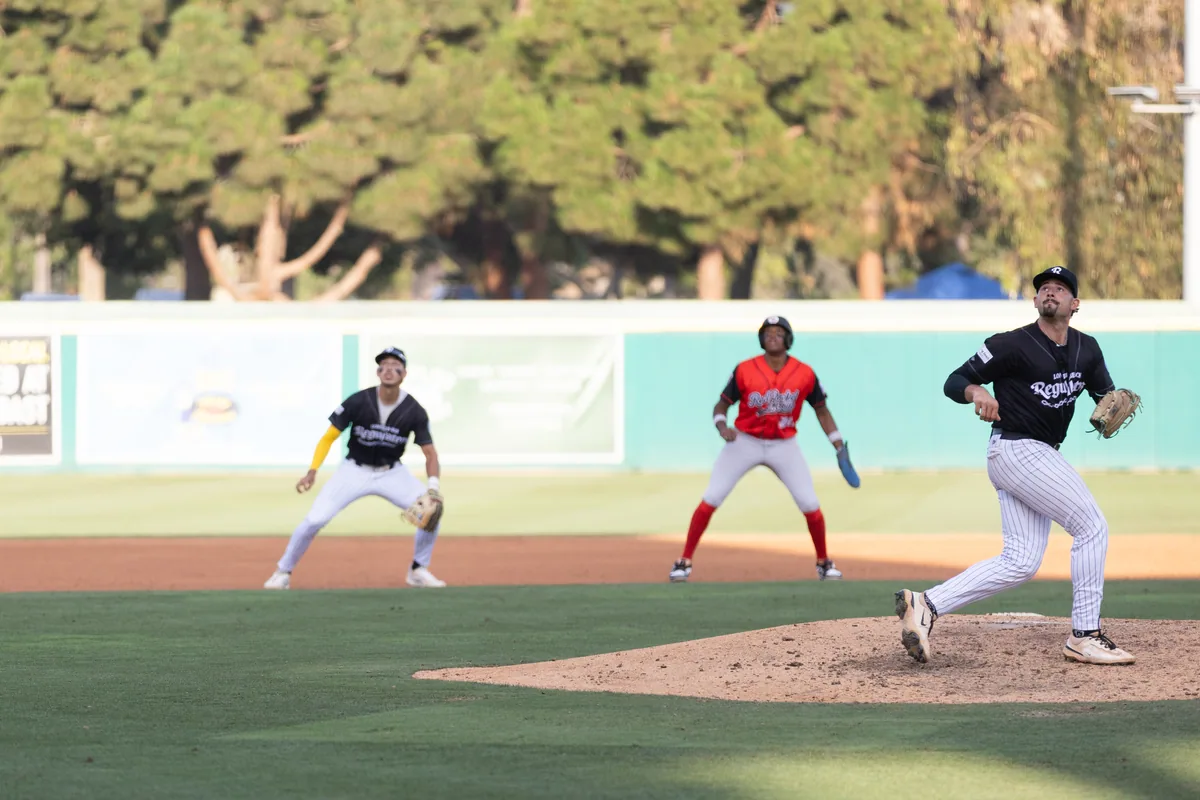 A pitcher mid-delivery with the empty grandstand beyond