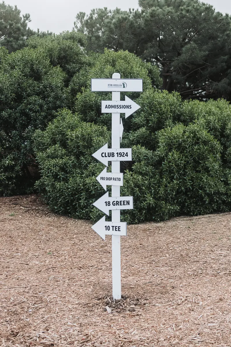 A white wooden signpost on the sand path directing players to the club yard, the 10th green and the 10th tee at Palos Verdes Golf Club