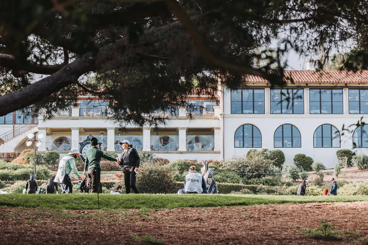 The Spanish Colonial clubhouse at Palos Verdes Golf Club in flat morning light, a group gathering on the lawn below the terrace