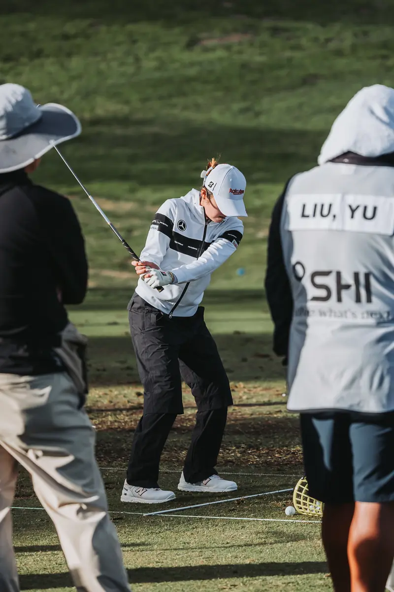 Caddie bibs at close range on the practice tee, a player mid-backswing between them