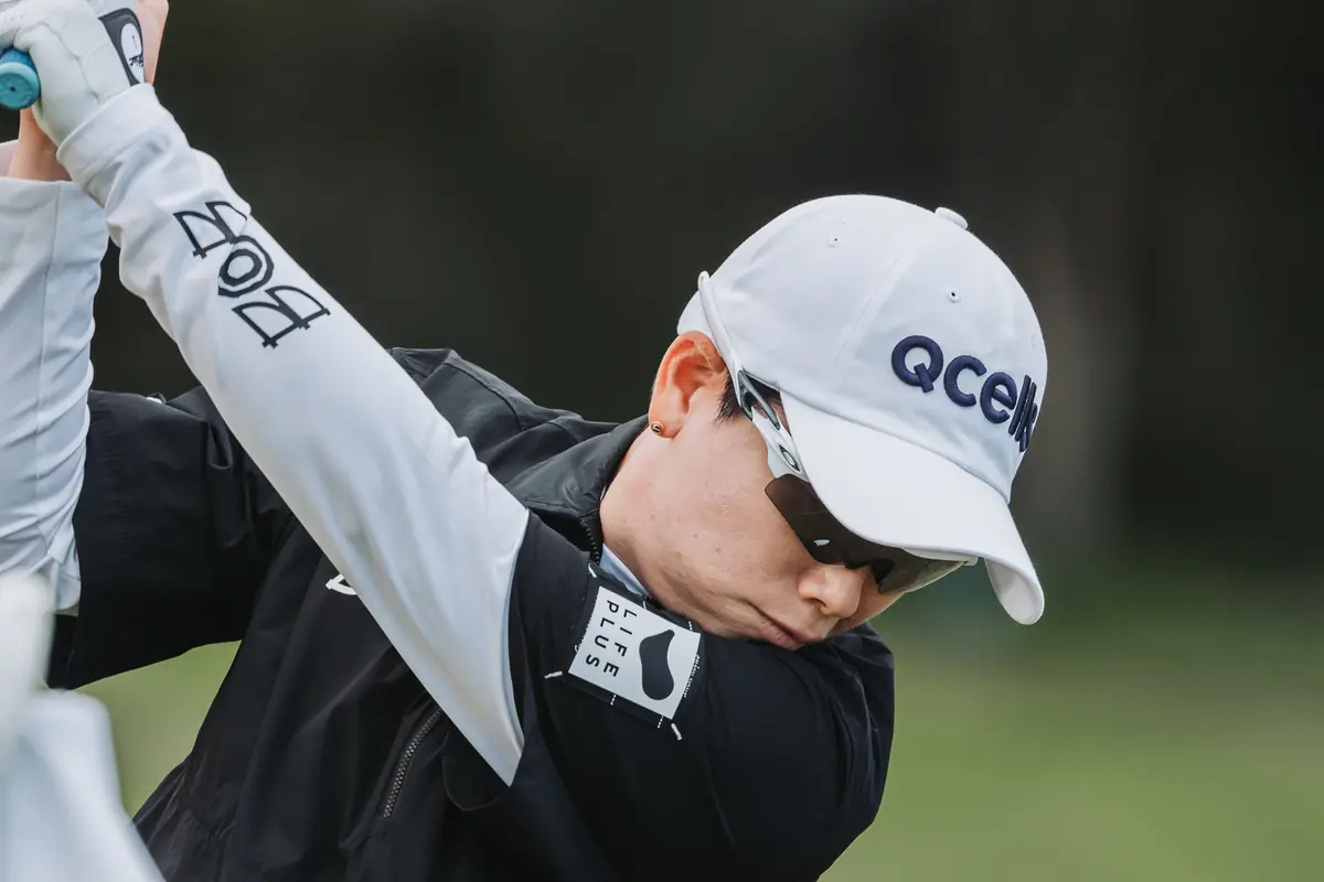 A player stretching with a club held overhead behind her shoulders in the cold morning air before her round