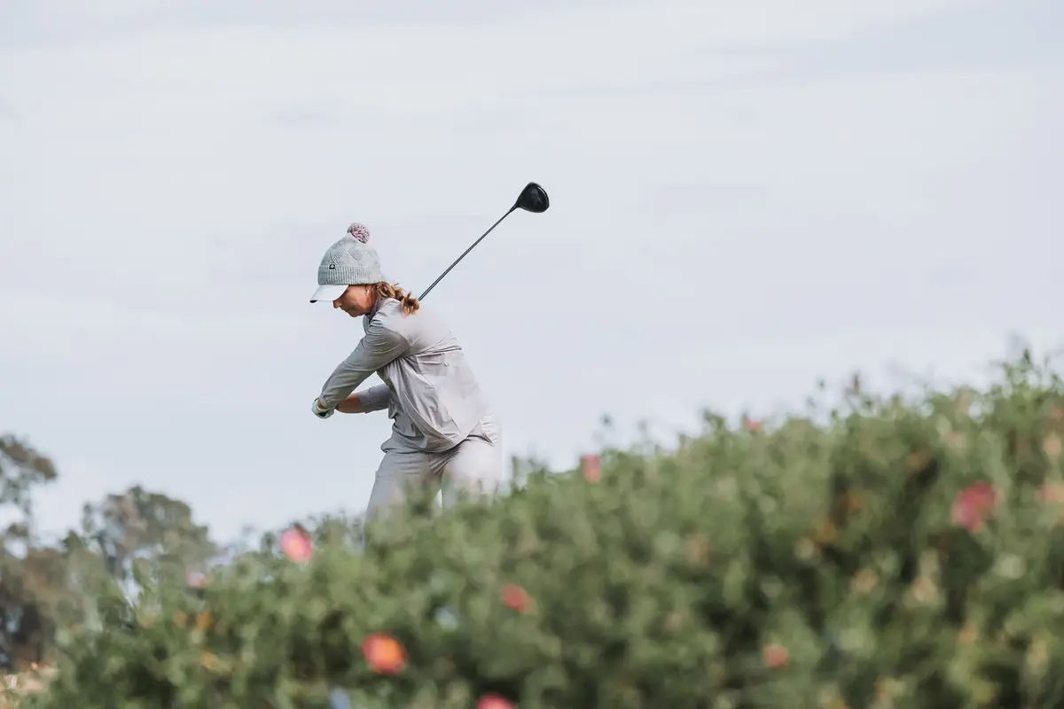 A driver swing framed low through red blossoms on the coastal bank