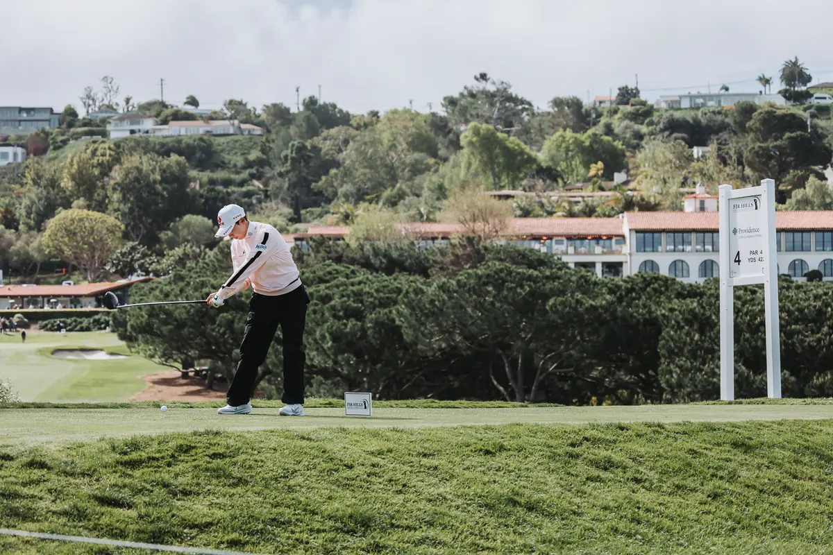 A player driving with the long tile roofline of the resort below the course behind her