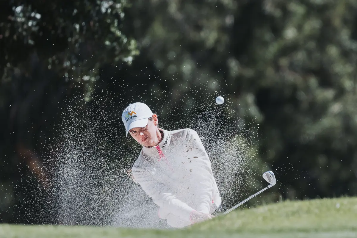 A backlit explosion of sand as a player plays out of a fairway bunker, ball already gone