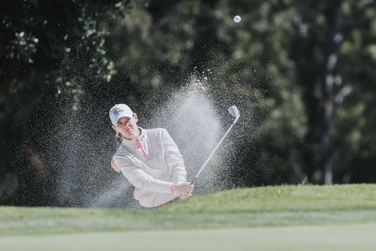 A player almost lost inside her own sand spray on a greenside recovery