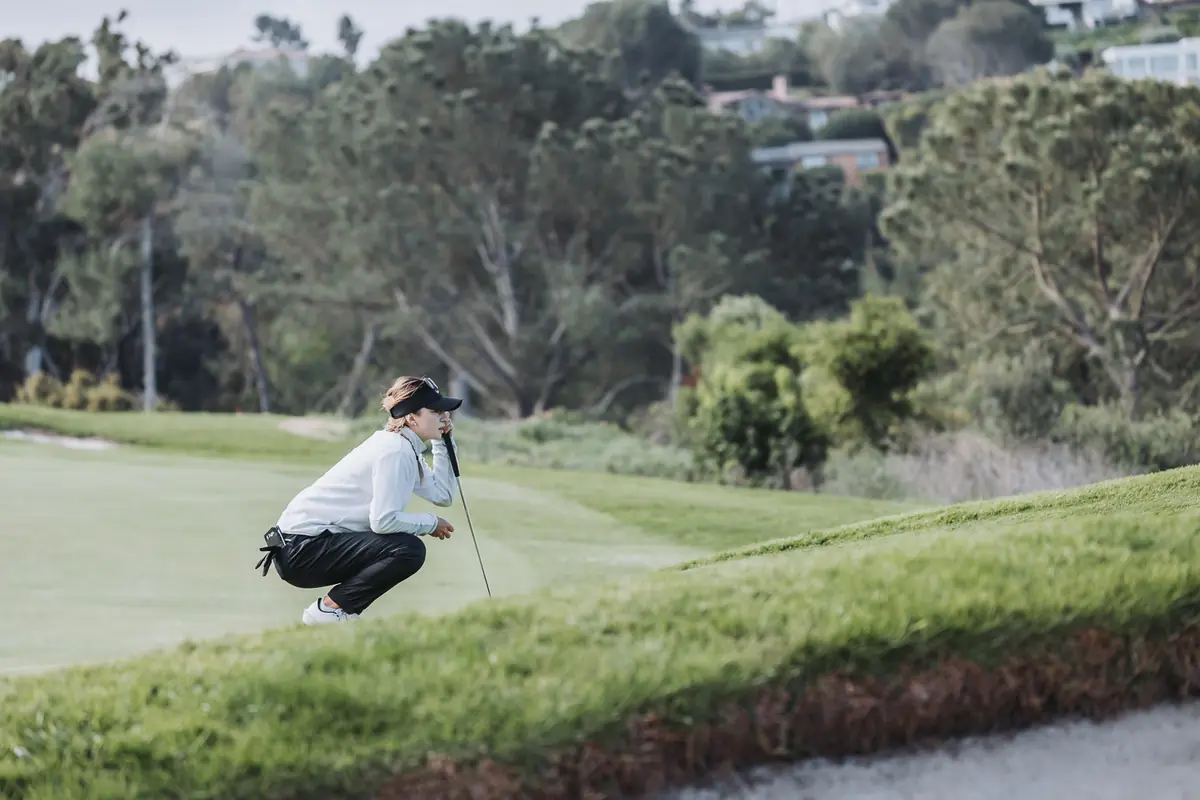 A player crouched to read her line on a green cut into the canyon edge at Palos Verdes Golf Club