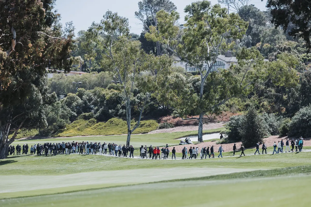 A long line of spectators walking the edge of the fairway behind the last group