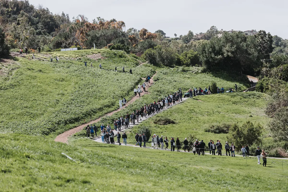 The crowd line curving along the canyon path, hundreds deep, seen from across the hole