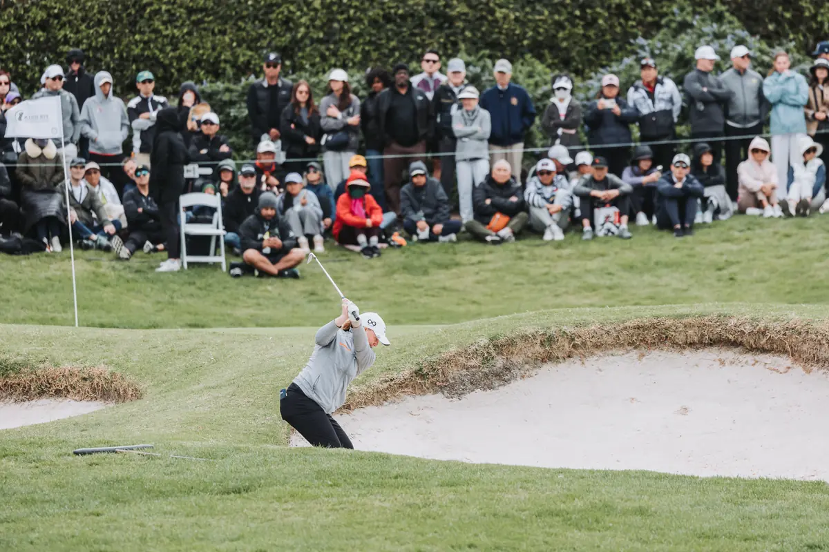 A greenside bunker shot played in front of a bank of spectators seated shoulder to shoulder on the slope
