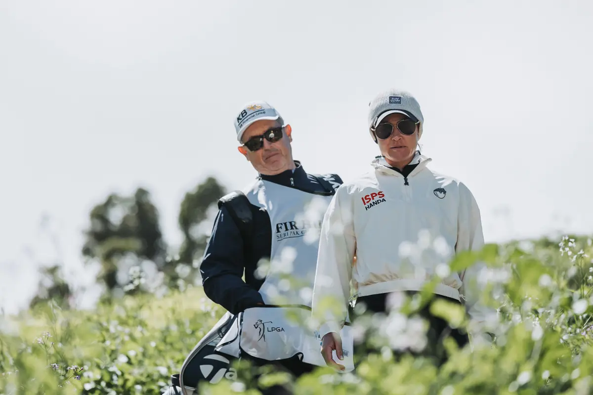 Two caddies walking a path framed by white coastal blossom at Palos Verdes Golf Club