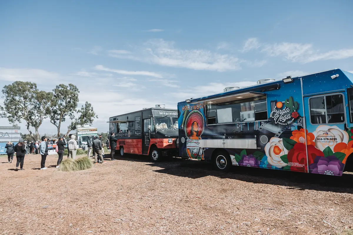 Shuttle buses and a painted food truck parked on the hard ground at the spectator entrance