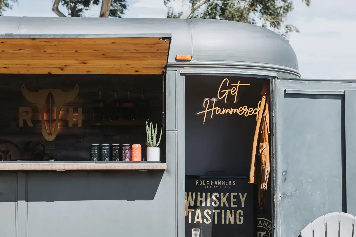 A converted horse trailer serving a whiskey tasting under a neon sign on the spectator route