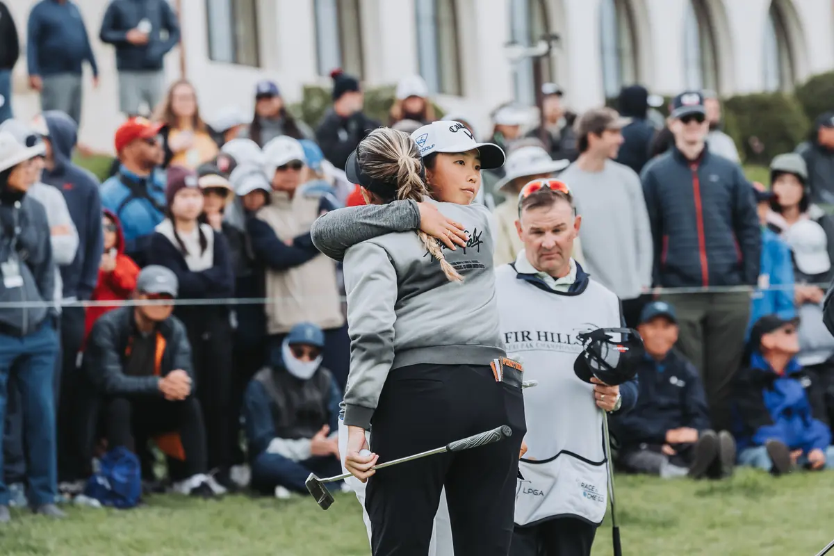 A player and her caddie holding on to each other on the green after the final putt, crowd behind them