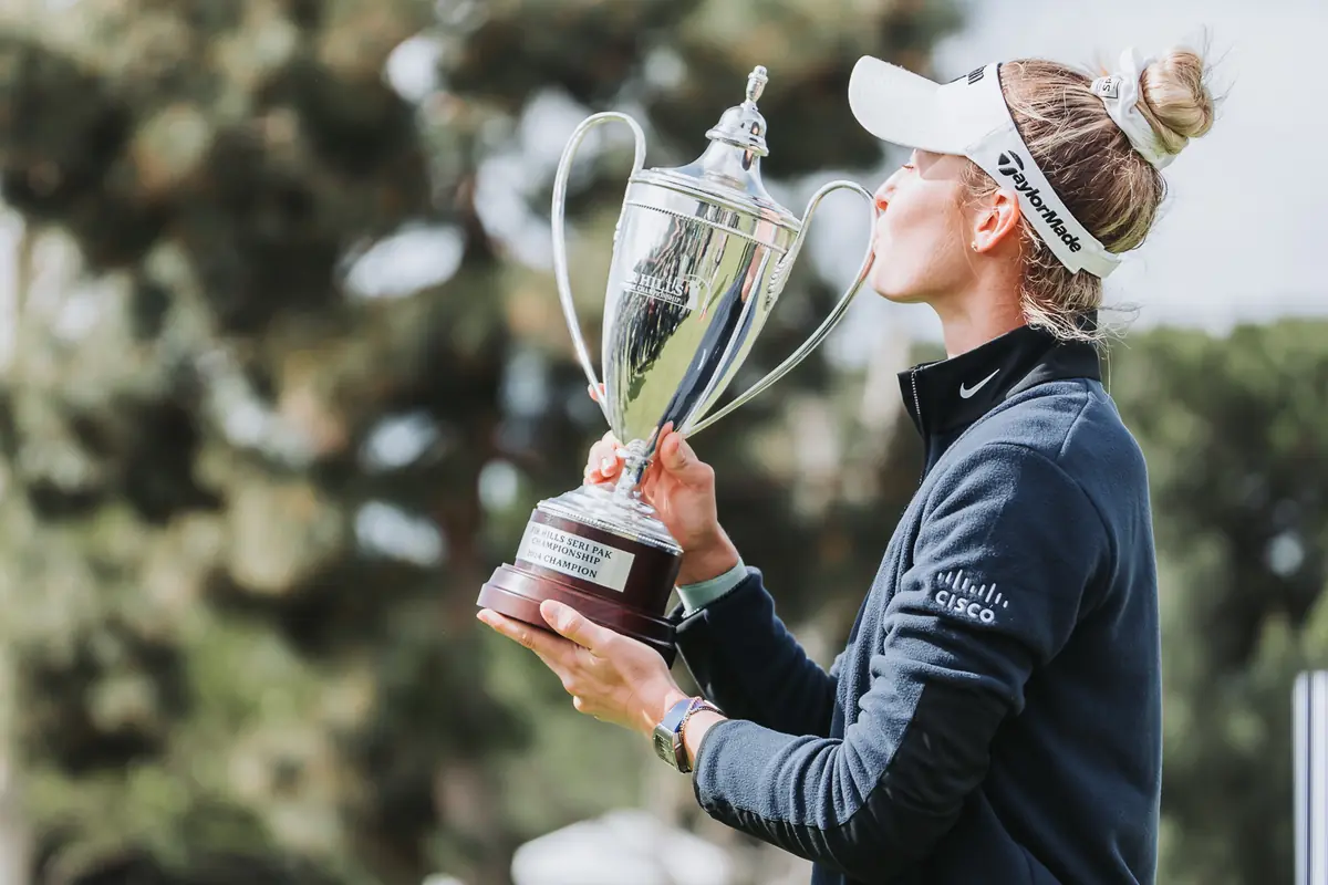 The champion lifting the trophy above her shoulder, looking up at it
