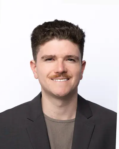 Team member in a charcoal blazer over a tan tee