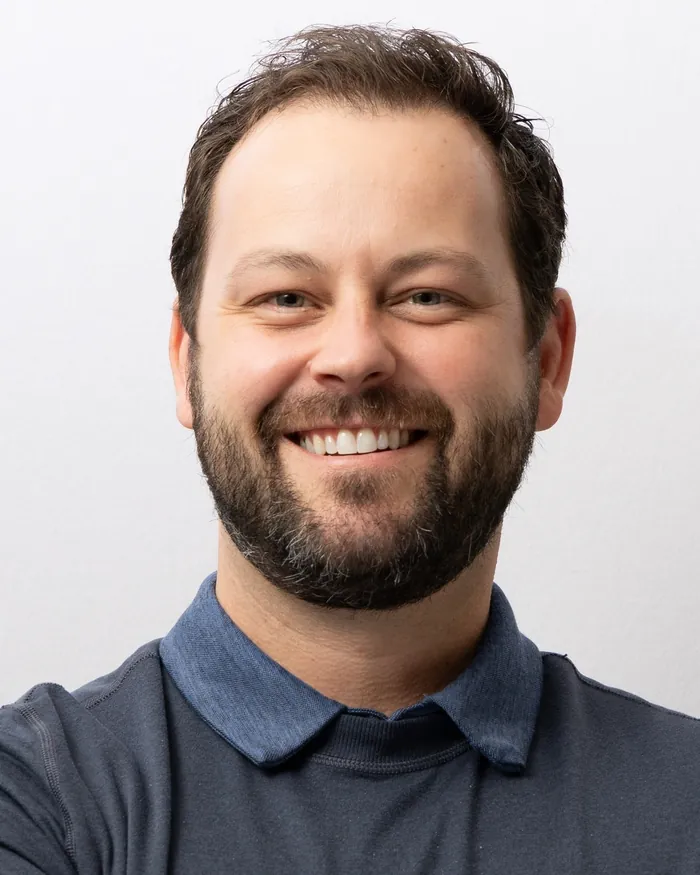 Team member in a slate polo with arms folded on the same white backdrop