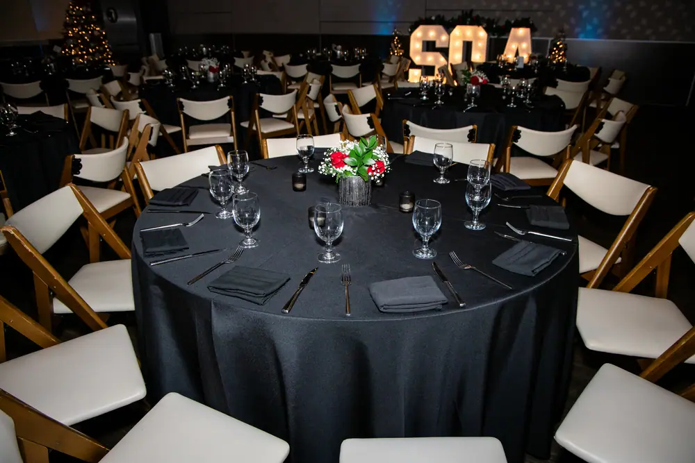A banquet round set with black linen, red centrepiece and the lit SQA letters glowing behind it