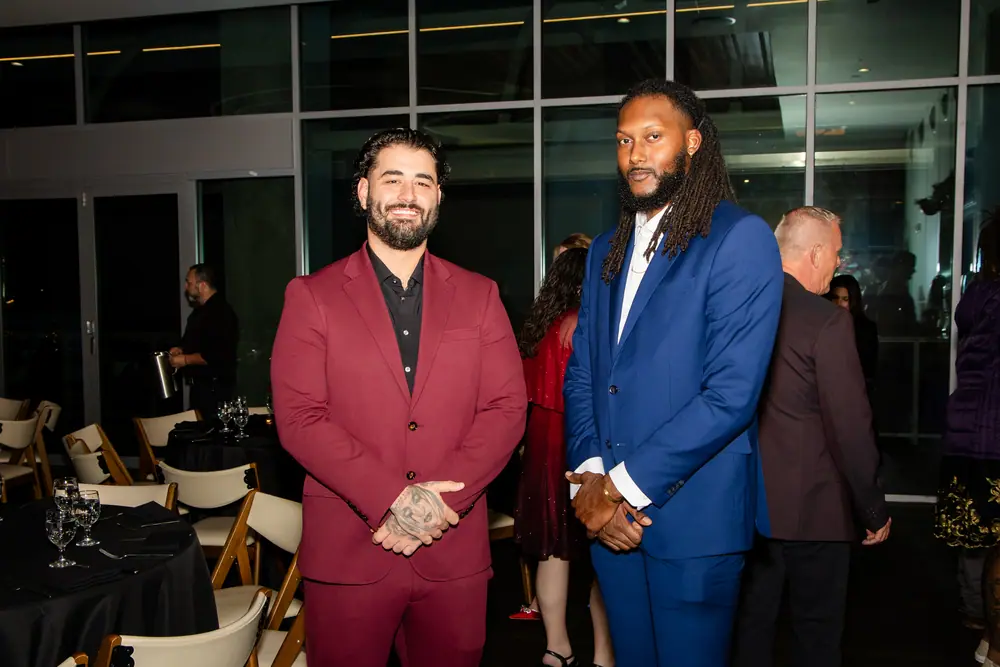 Two guests in a burgundy suit and a cobalt suit standing together by the Sky Level windows