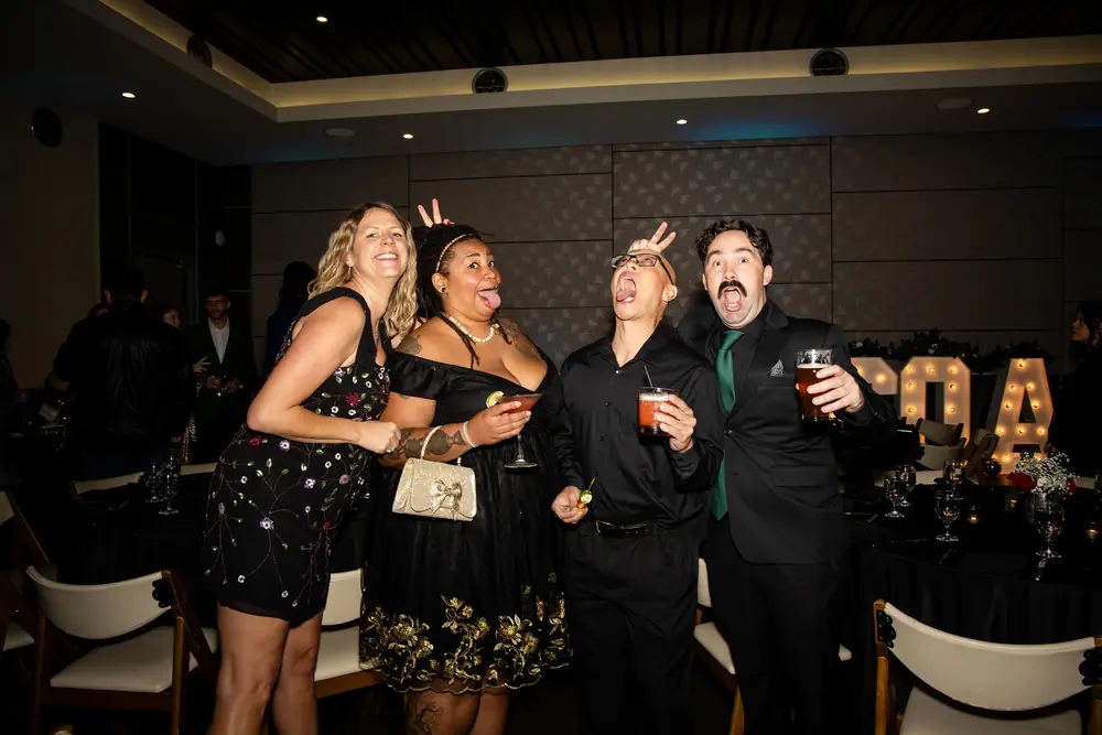 A group of SQA Services guests pulling faces in front of the lit SQA marquee letters, drinks in hand