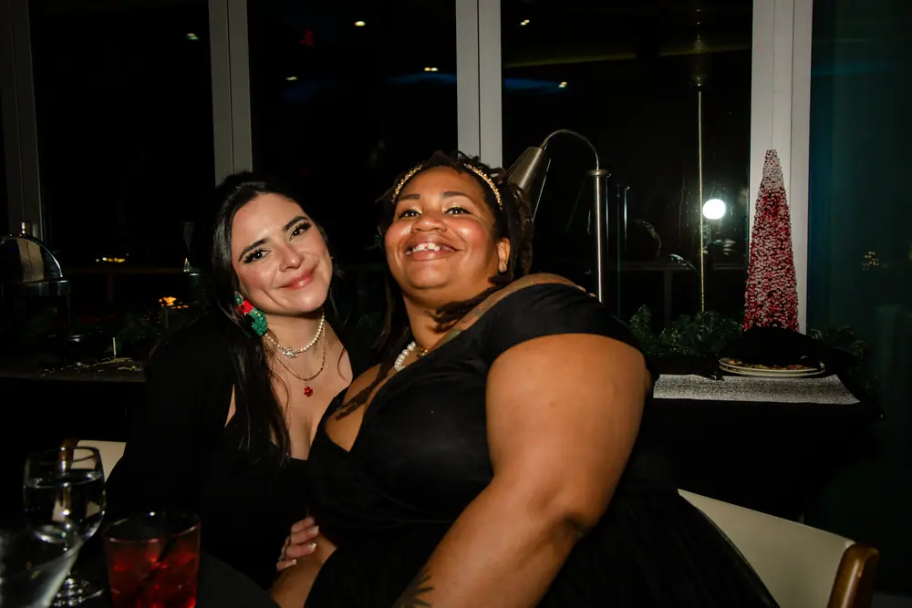 Two colleagues leaning in together at the window, both laughing, at the SQA Services holiday party