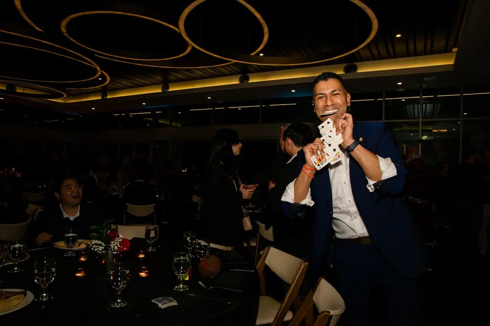 The magician fanning a deck of cards over a dinner table beneath the gold ring chandeliers