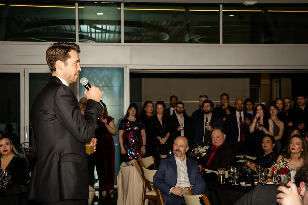 An SQA Services executive giving the 30th anniversary remarks into a handheld microphone, the standing room behind him