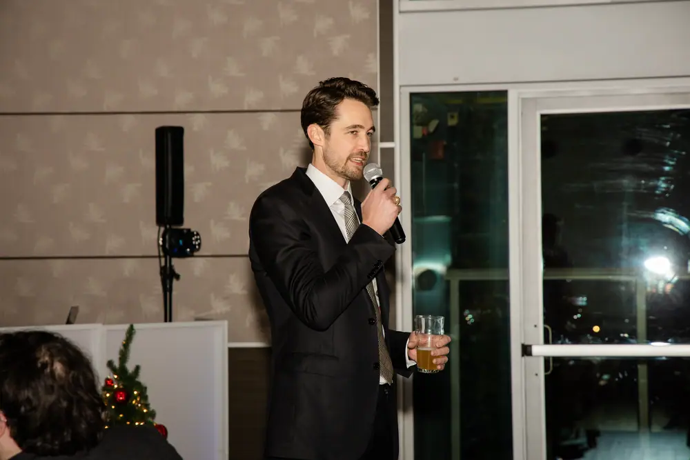 The speaker mid-sentence with a microphone, lit against the Sky Level window wall