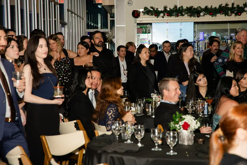 Guests at the front tables listening to the anniversary remarks, drinks down