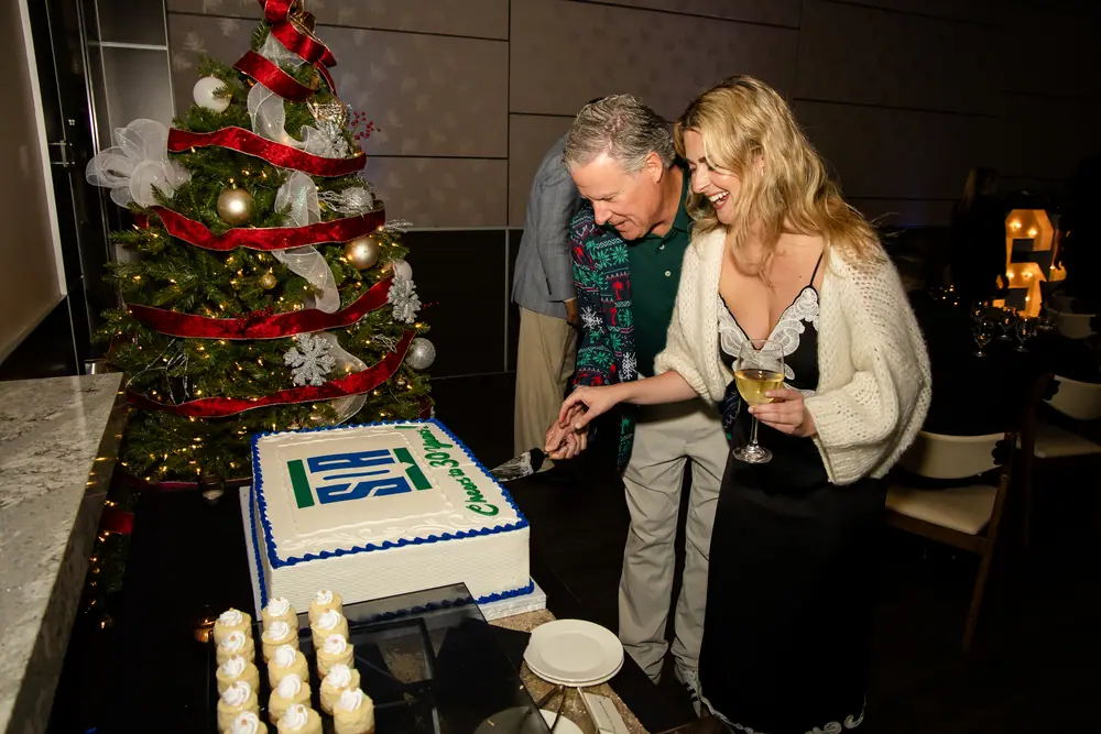 Two SQA Services colleagues cutting the 30th anniversary cake together, both laughing