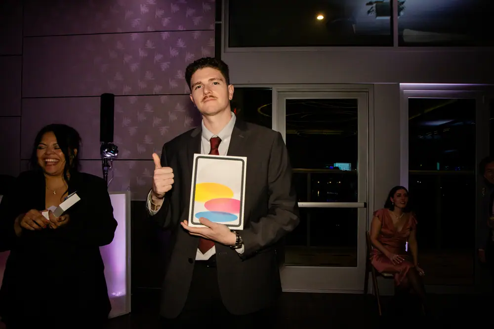A raffle winner holding up a tablet in its box and giving a thumbs up at the SQA Services party