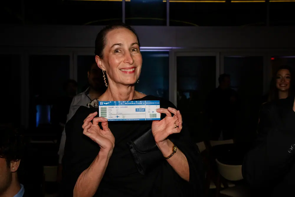 A guest smiling as she holds up a mock boarding pass she has just won in the raffle