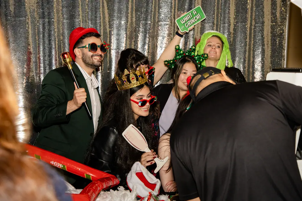 Photo booth in full swing in front of a silver sequin backdrop — crowns, wigs and holiday props