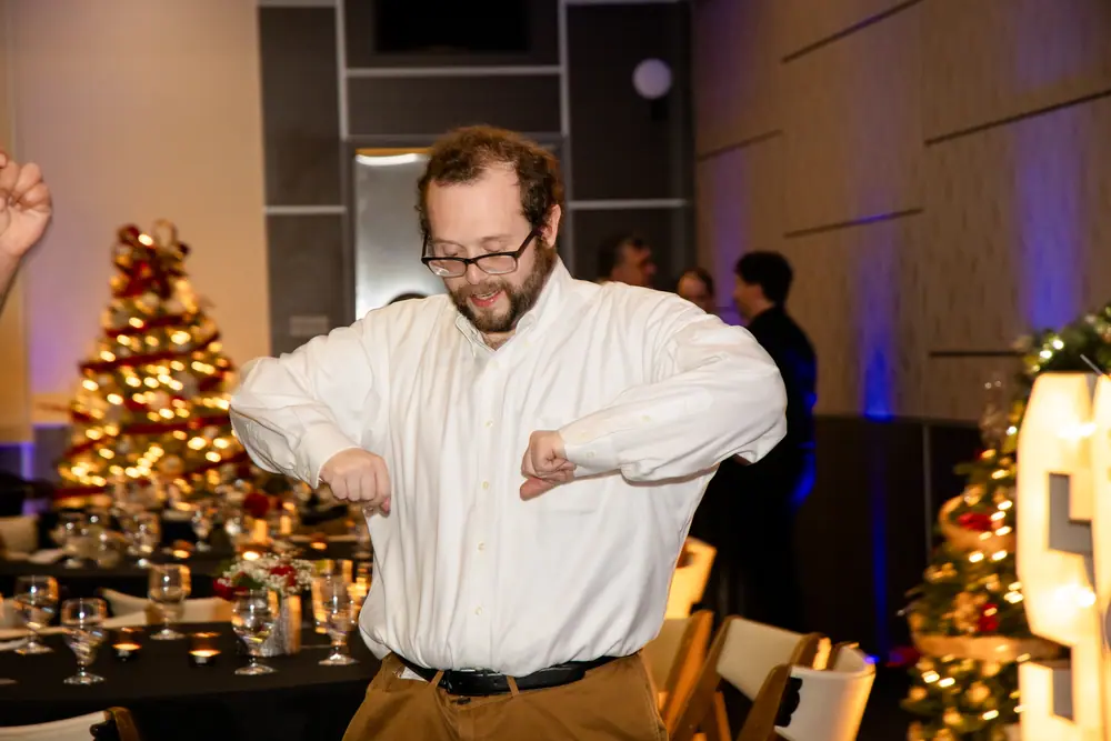 A guest dancing alone by the Christmas trees, elbows tucked, entirely committed