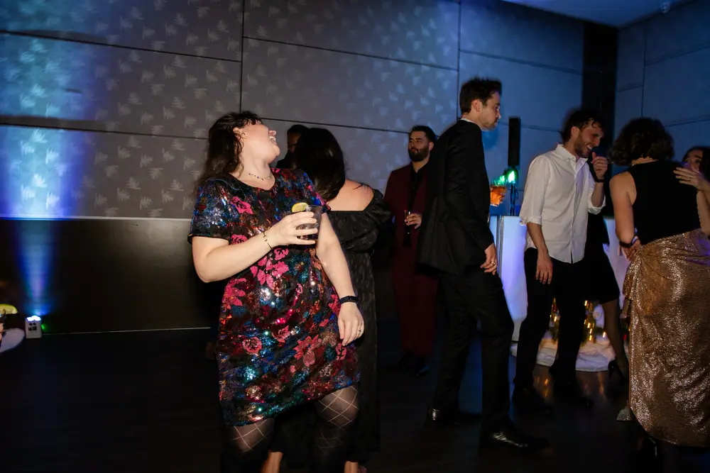 A guest dancing with her head thrown back mid-laugh, drink still in hand, the floor busy behind her