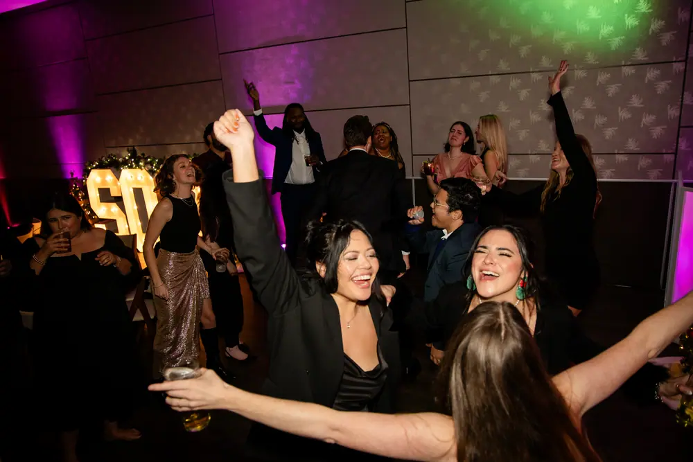 Arms overhead on a magenta-lit dance floor with the SQA marquee letters glowing behind